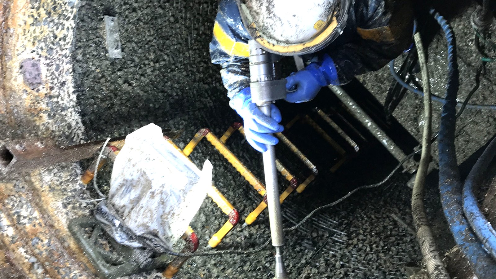 マンホール内部を上から見た様子。ヘルメットの作業員が細いランスを構え、足元には既設の鉄はしごと配管が見えている